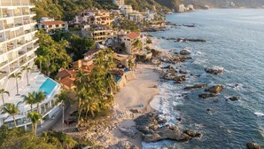 Un pueblo costero con playa, costa rocosa y edificios con balcones que dan al mar.