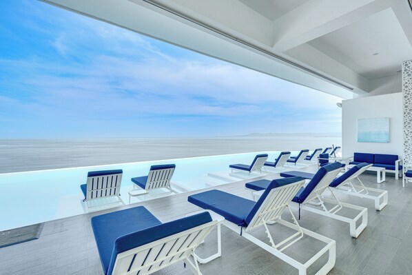 A modern indoor pool area with lounge chairs and a view of the ocean.