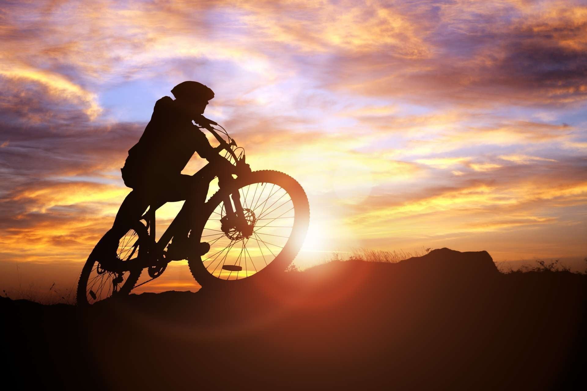 La silhouette d’une personne à vélo, se détachant sur le ciel au coucher du soleil.