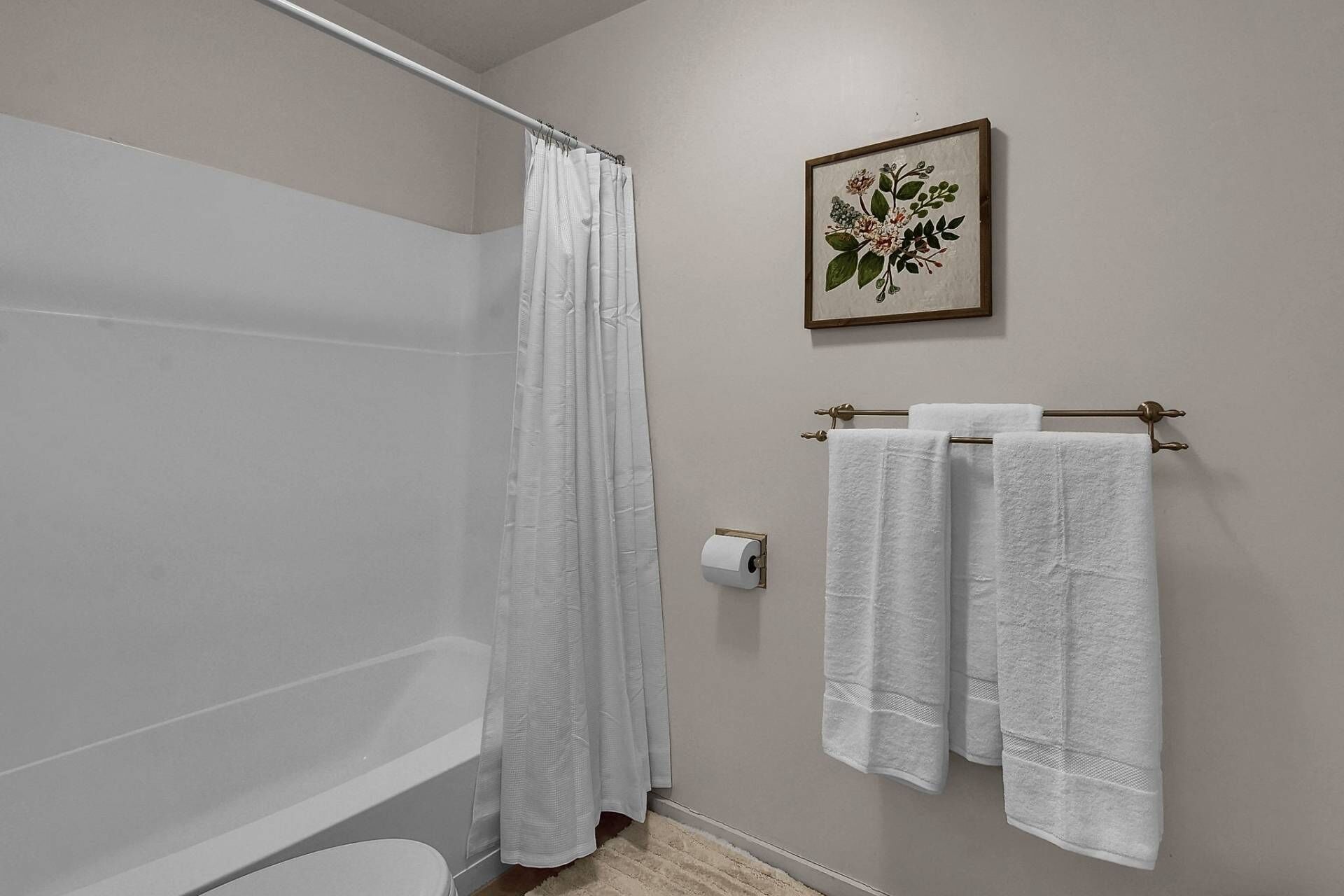Une salle de bain avec un rideau de douche, des toilettes, un porte-serviettes avec deux serviettes et une œuvre d’art florale encadrée au mur.