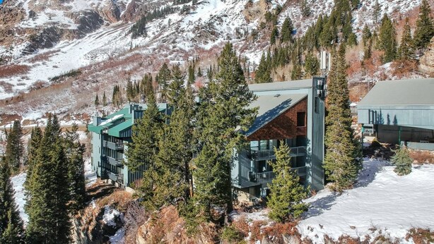 A modern mountain lodge with a glass facade, surrounded by snow-covered terrain and dense forest. - Great Weekend Destination-Between Snowbird & Alta, Hot Tub, BBQ, Free Parking, Free Ski Rental (Alta)