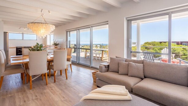 A modern living room with a large window, a dining area, and a cozy sofa. - Coastal home in Gracetown - relaxing! (Gracetown)