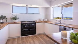 A modern kitchen with white cabinets, a black stove, wooden countertops, and large windows offering a view of the sea. - Coastal home in Gracetown - relaxing! (Gracetown)