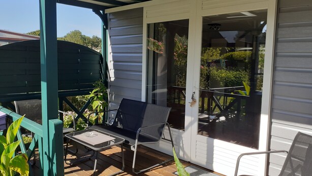 A covered patio with a table and chairs, a sliding glass door, and a view of the garden. - Chalet 100 m from the little sea of Gâvres (Riantec)