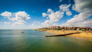 Escena costera con playa, muelle que se adentra en el agua y edificios al fondo.