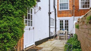 A narrow courtyard with a white door, a brick wall, and a small table with chairs. - Charming 3 bedroom cottage in heart of Southwold (Southwold)