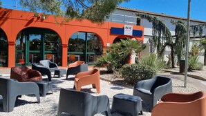 An outdoor seating area with plastic chairs and tables in front of a building with an orange facade and a sign that reads "ACE HOTEL." - ACE Hôtel Travel Fabrègues - A9 Montpellier Sud (Fabregues)
