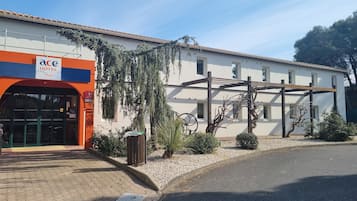 L’entrée d’un hôtel, avec une enseigne indiquant « ACE HOTEL, voyages », et un espace extérieur abrité avec des sièges.
