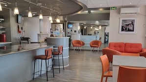 A modern bar area with a curved counter, orange chairs, and a seating area with a table and chairs. - ACE Hôtel Travel Fabrègues - A9 Montpellier Sud (Fabregues)