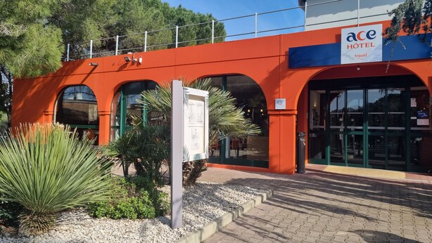 A hotel entrance with a red facade, a signboard, and a pathway leading to the entrance. - ACE Hôtel Travel Fabrègues - A9 Montpellier Sud (Fabregues)