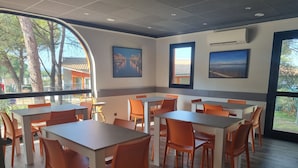 A dining area with tables and chairs, large windows, and artwork on the walls. - ACE Hôtel Travel Fabrègues - A9 Montpellier Sud (Fabregues)