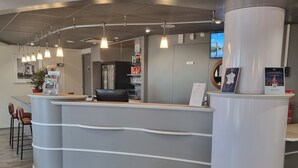 A modern reception desk with a curved design, a digital screen, and a seating area with chairs. - ACE Hôtel Travel Fabrègues - A9 Montpellier Sud (Fabregues)