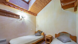 Una stanza con due letti in legno, un comodino in legno, una lampada a parete e un lucernario.