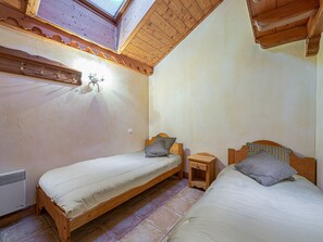 Ein Zimmer mit zwei Holzbettgestellen, einem kleinen Nachttisch aus Holz, einer Wandleuchte und einem Oberlicht.
