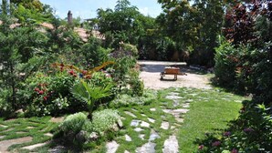 A garden with a stone pathway, a wooden bench, and various plants. - Classic Double Room: Double studio, with capacity for two people. (Olmedo)