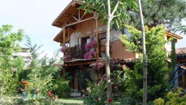 A wooden house with a balcony, surrounded by lush greenery and flowers. - Basic Triple Room: Private entrance and porch (Olmedo)