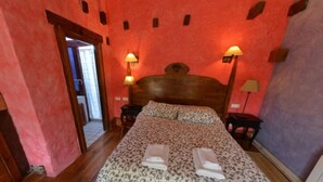 A bedroom with a wooden headboard, two bedside lamps, a patterned bedspread, and a visible door leading to another room. - Basic Triple Room: Private entrance and porch (Olmedo)