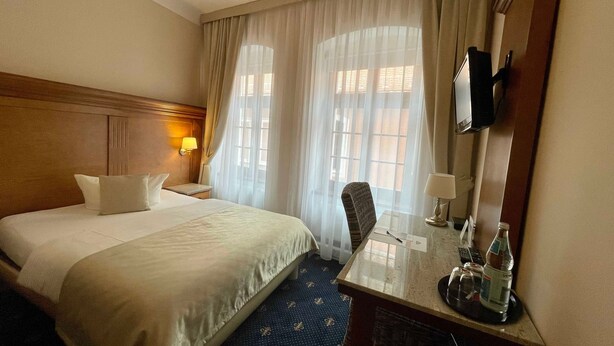 Una habitación de hotel con una cama grande, un escritorio con una silla, un televisor y una ventana con cortinas.