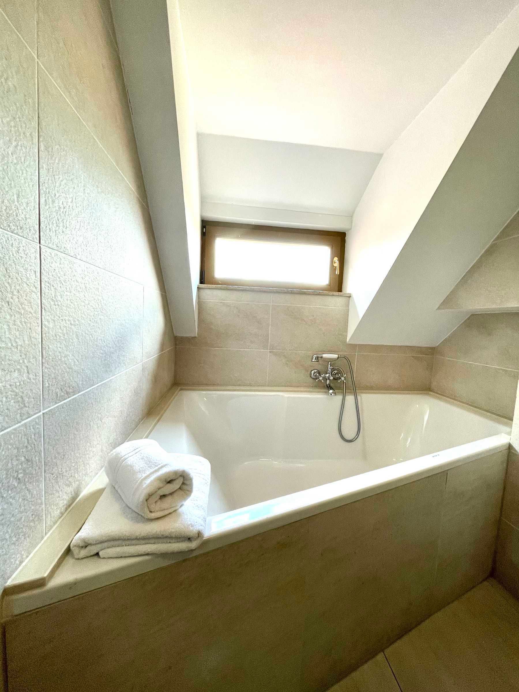 A modern bathroom with a freestanding bathtub, a towel, and a small window above the tub.