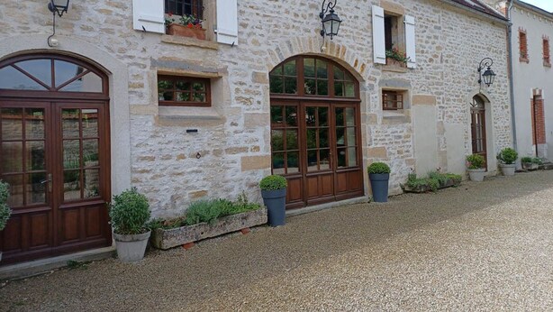 A stone building with arched windows and doors, potted plants, and a gravel driveway.