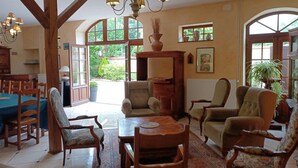 A spacious room with a dining area, multiple seating options, and large windows providing natural light.