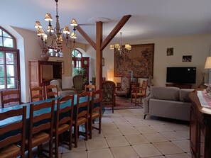 Uma sala de estar ampla com área de jantar, móveis de madeira, um lustre e uma grande pintura na parede.