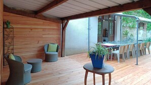 An outdoor patio with wooden flooring, wicker furniture, and a table with a potted plant.