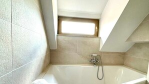 Een moderne badkamer met een vrijstaand bad, een handdoek en een klein raam boven het bad.