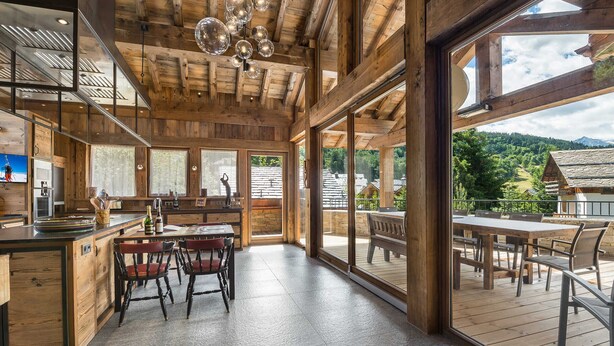 A spacious kitchen with wooden beams, large windows, and a dining area with a view of the surrounding landscape. - Luxury Chalet 7 Bed, Pool & Hammam, Pets Allowed (Méribel)