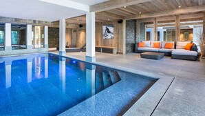 A spacious indoor pool area with a clear view of the pool, wooden beams, and a seating area with cushions. - Luxury Chalet 7 Bed, Pool & Hammam, Pets Allowed (Méribel)