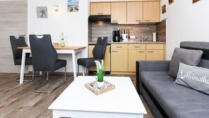 Una sala de estar moderna con un sofá gris, una mesa de centro blanca y un comedor con una mesa blanca y sillas negras.