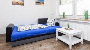 Una habitación moderna con un sofá cama azul, paredes blancas y dos cuadros enmarcados.