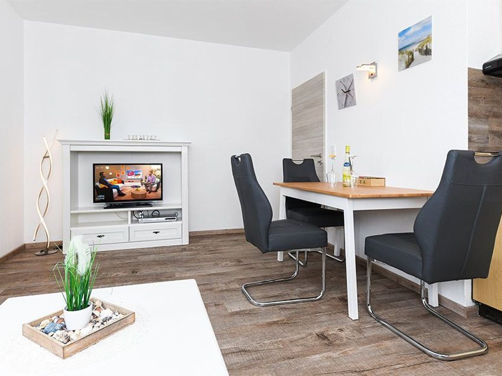 Ein stilvoller Essbereich mit Holztisch, schwarzen Stühlen, einem Fernseher auf einem weißen Schrank und einer kleinen Pflanze auf dem Boden.