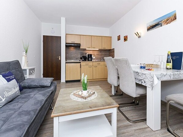 Um espaço de estar compacto com sofá, mesa de jantar e área de cozinha.