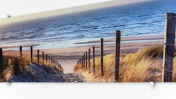 Ein Strandbild mit einer Holzlattenzaun und Gras im Vordergrund, das zum Meer führt.