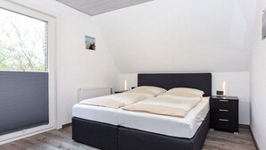 Ein Schlafzimmer mit einem Bett, einem Nachttisch, einem Fenster mit Jalousien und einer Heizung.
