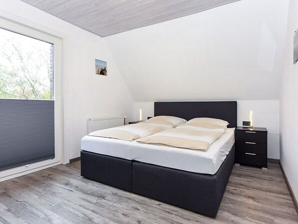 A bedroom with a bed, a nightstand, a window with blinds, and a radiator.