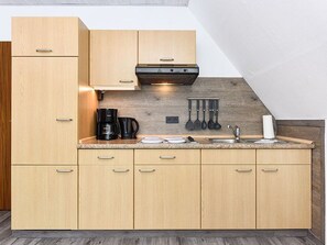 A modern kitchen with light wood cabinets, a stainless steel range hood, and a granite countertop.