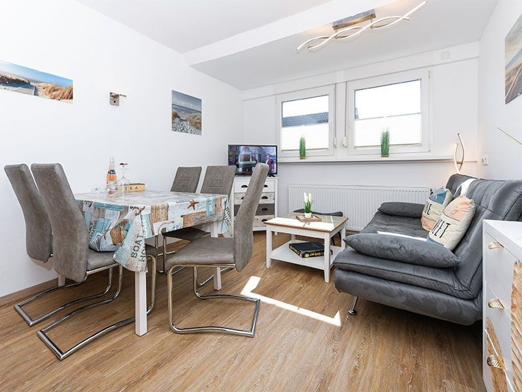A modern living room with a grey sofa, a dining table with chairs, and a TV.