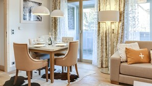 En matplats med ett bord för fyra personer, en soffa och ett stort fönster med gardiner.