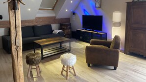 Un salon chaleureux avec un canapé, un fauteuil, une table basse et un téléviseur posé sur un meuble en bois.