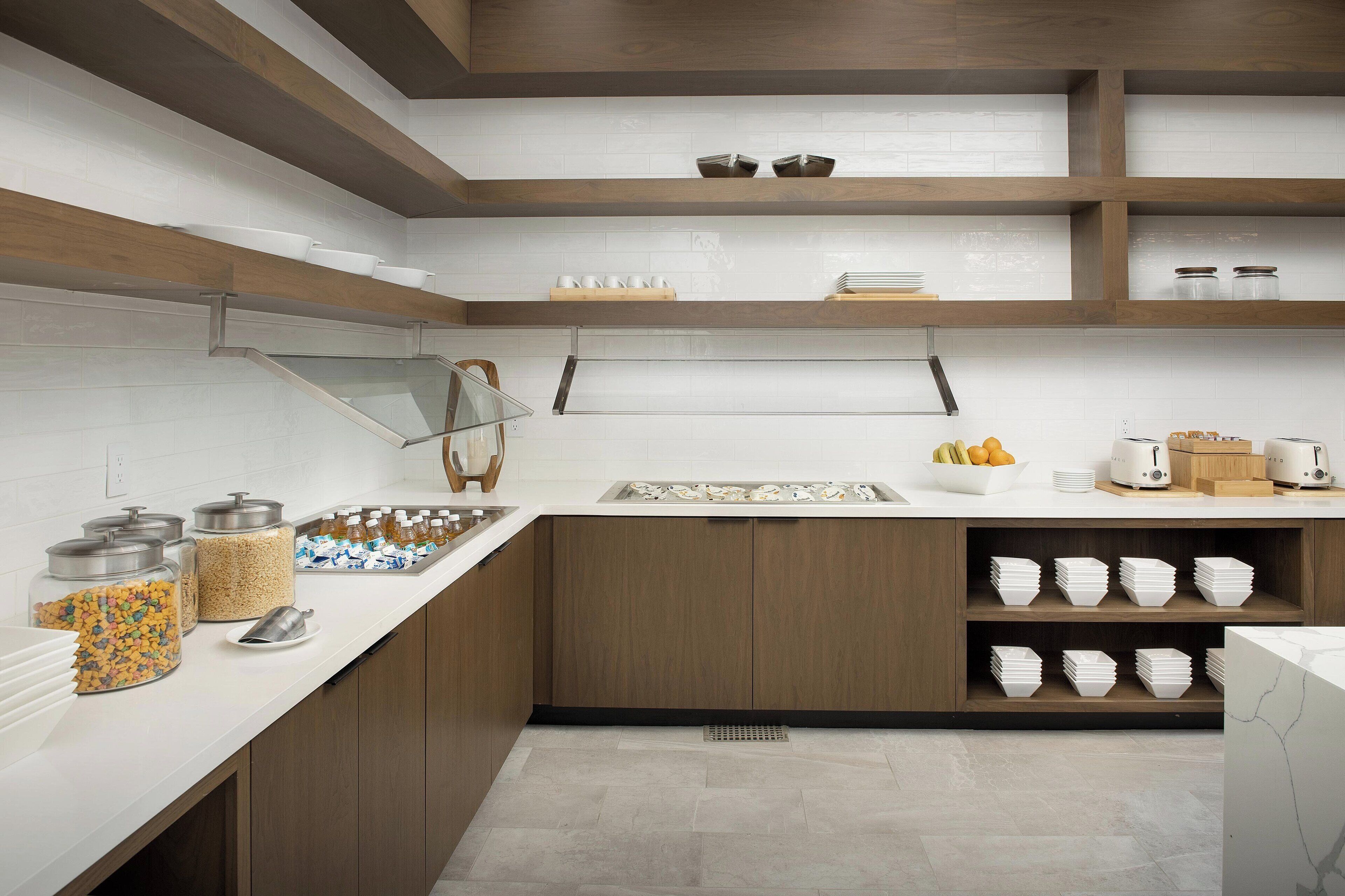 A modern kitchen with white countertops, wooden cabinets, and a built-in shelf with bowls and cups.