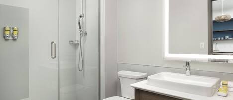 A modern bathroom with a glass shower enclosure, a white toilet, and a vanity with a mirror above the sink.