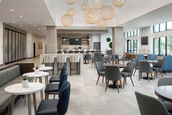 A modern hotel lobby with seating areas, a bar, and a kitchen in the background. - Element by Marriott Seattle Sea-Tac Airport (Tukwila)