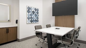 Une salle de conférence avec une table blanche, six chaises, un grand écran et une œuvre d’art abstraite encadrée accrochée au mur.