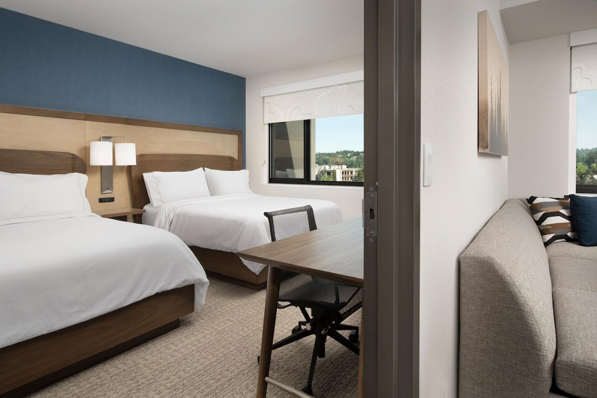 A hotel room with two beds, a desk, and a sofa.