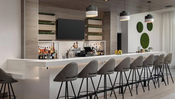 A modern bar area with a long counter, multiple stools, and a flat-screen TV mounted on the wall. - Element by Marriott Seattle Sea-Tac Airport (Tukwila)