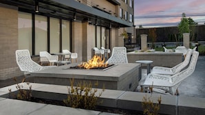 An outdoor seating area with a fire feature, white wicker chairs, and a modern building in the background. - Element by Marriott Seattle Sea-Tac Airport (Tukwila)