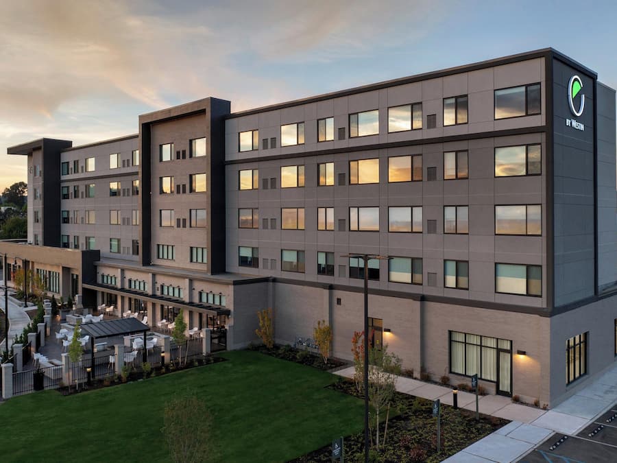Un hôtel moderne, composé de plusieurs étages, doté d’un espace extérieur couvert avec des sièges et d’un parking.