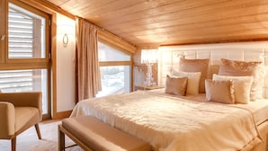 Un dormitorio con una cama grande, una mesita de noche con lámpara, una silla y una ventana con cortinas.